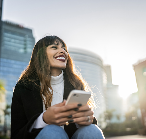 Smiling woman sitting outside the building holding phone
