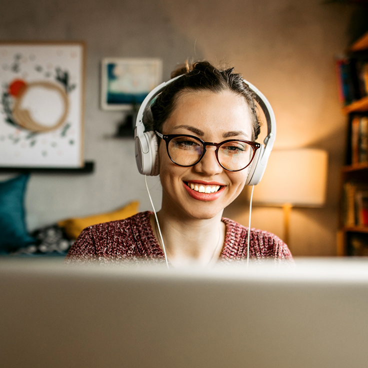 Young woman with glasses and headphones looking at a laptop screen