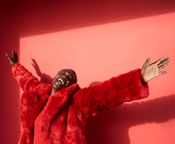 A woman in a red fake-fur coat raises her hands in happiness